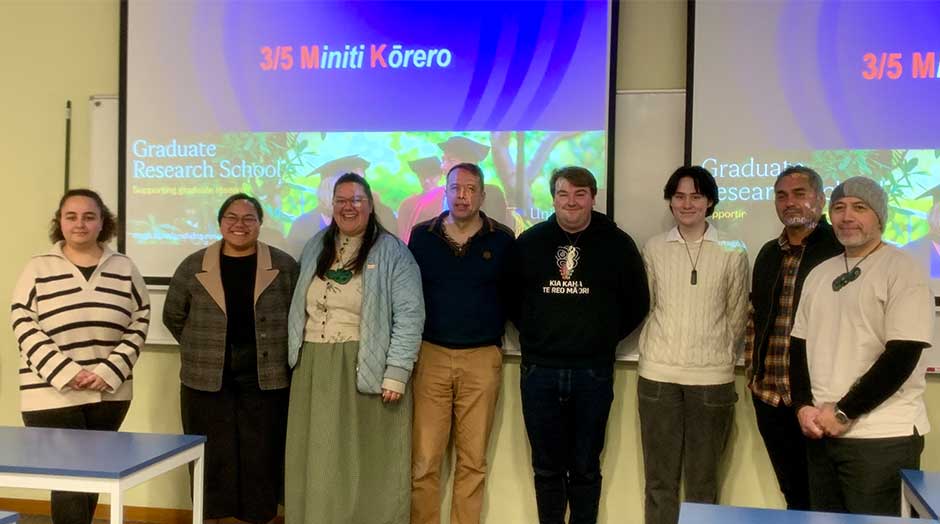 Eight people standing next to each other in front of whiteboards with '3/5 Minit Kōrero' on them