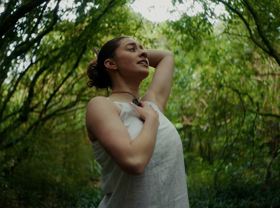 A young woman dancing with greenery behind her. 