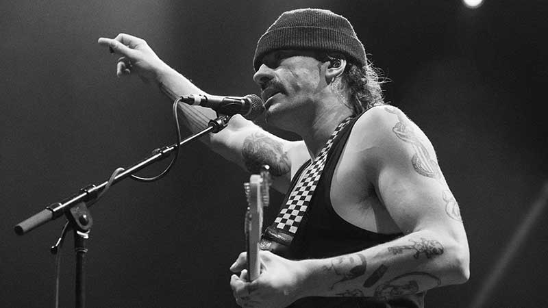 A man standing holding a guitar, wearing a hat, black and what image