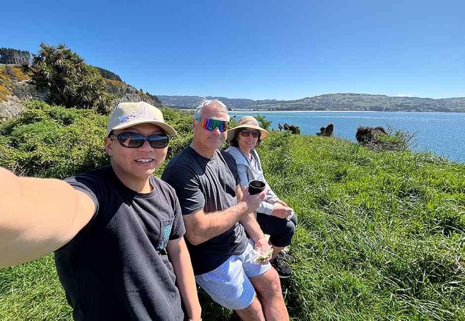 Student with homestay host family sit with view of Otago Peninsula in the background.