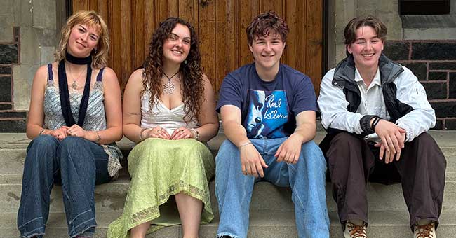 four young people seated on steps at the front of the Clocktower building 