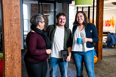 Three postgraduate students chatting, one holding a mug.