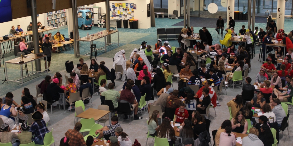 A large room full of huddled groups at individual tables taking part in a quiz.