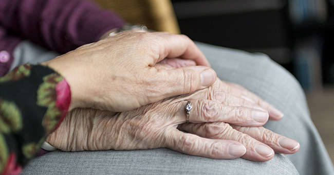 Photograph of an elderly person's hands, with a younger person's hand resting on top of them in a comforting gesture