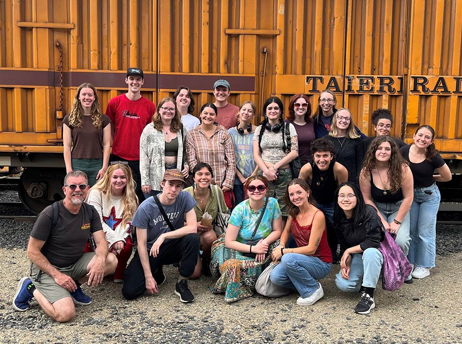 A large group of people sitting and standing in front of a railway carriage