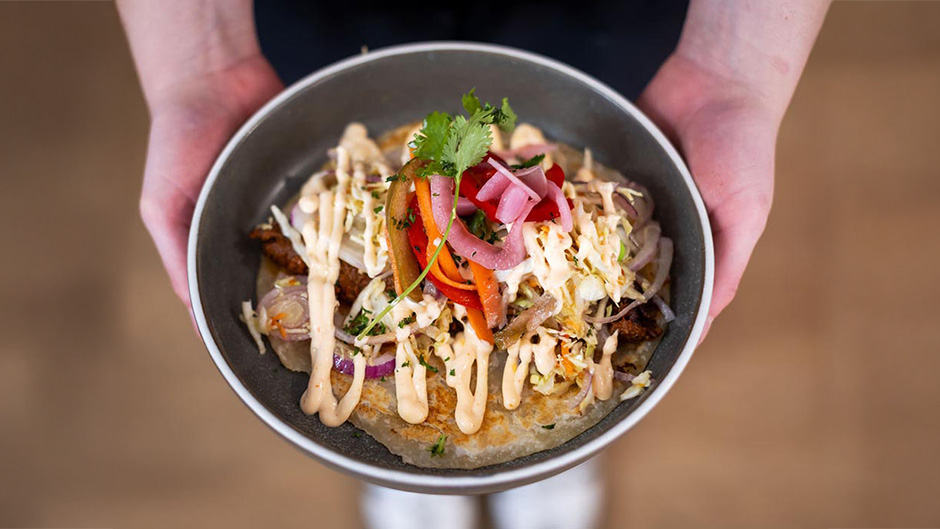 A close-up of a bowl of roti flatbread covered in fresh fillings
