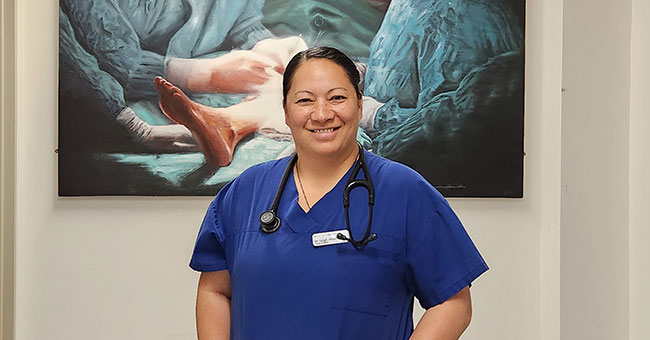 A female doctor standing in front of a painting of two doctors operating. 