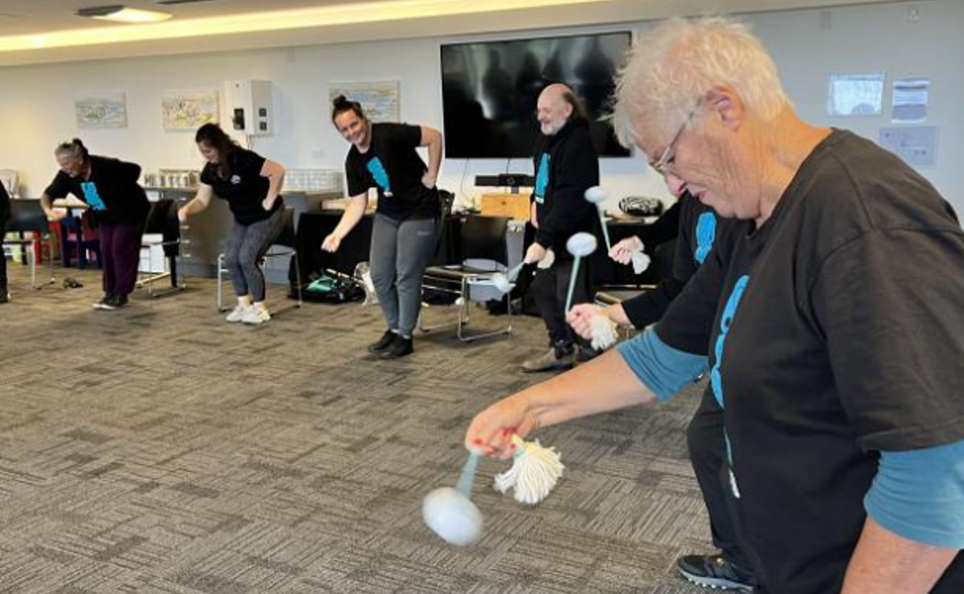 Instructors lead elderly patients in a large room in dancing with poi.
