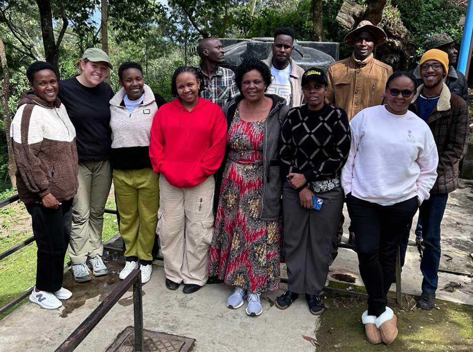 A group of people standing together on concrete with trees and greenery behind them
