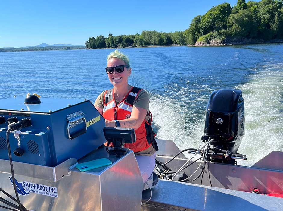 A woman steering a boat on water on a nice sunny day with land in the background