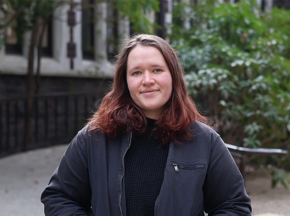 A woman is pictured in front of a stone building and ferns.