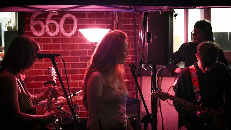 Four backlit, shadowy people performing with a brick hall behind them, 660 painted on the wall
