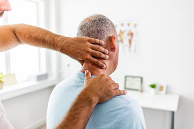 Person examining the neck and shoulder of a seated man.