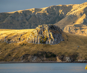 Basalt outcrops at Purau Bay, Banks Peninsula forming part of the 5.8-8.1Ma Diamond Harbour Volcanic Group. The Port Hills in the background are composed of an older 9.7-11Ma sequence.