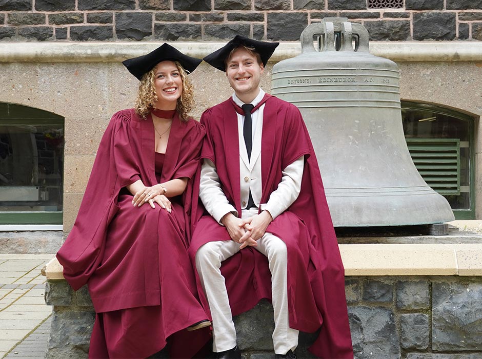 Emma-Anderson-and-Ben-Sutherland-next to bell in Uni Quad