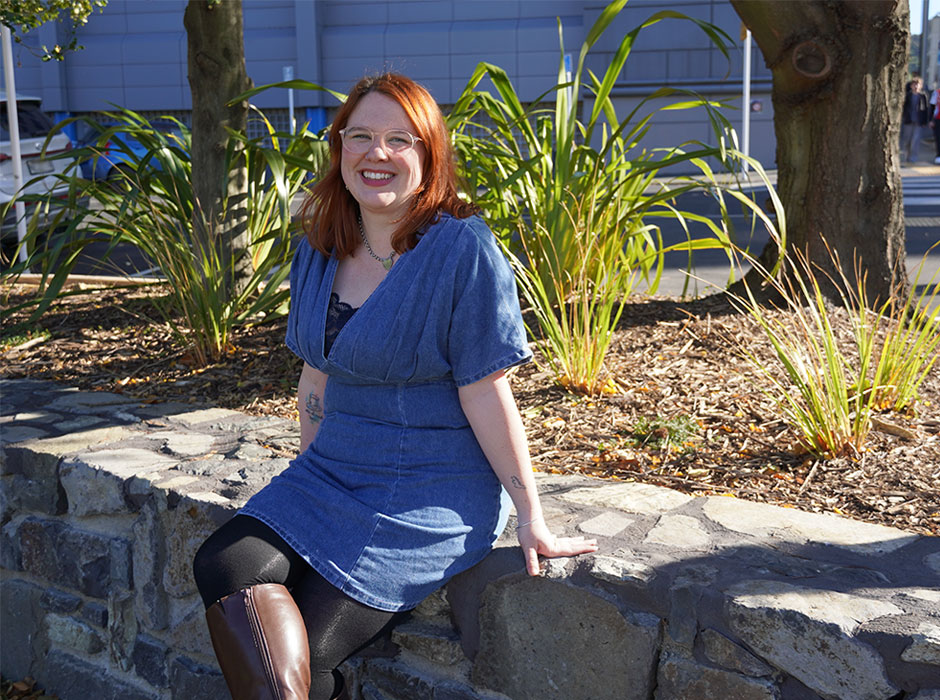 A woman posing in a garden, seated on a low wall