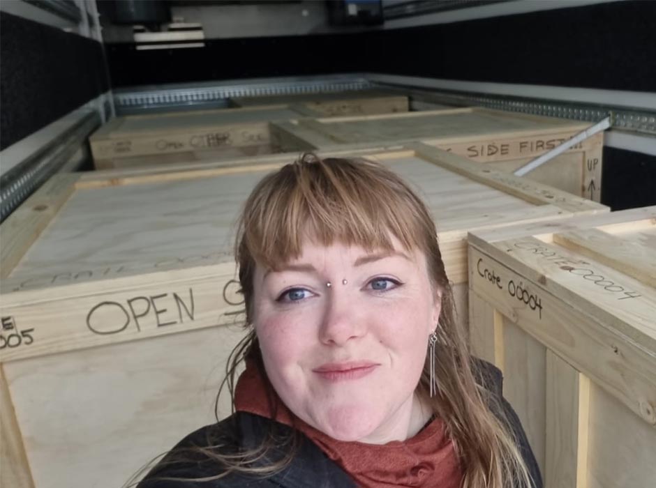 A woman stands in front of a crate.