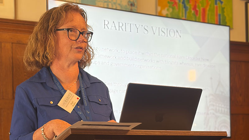 A woman standing at a podium with a presentation on the screen behind her