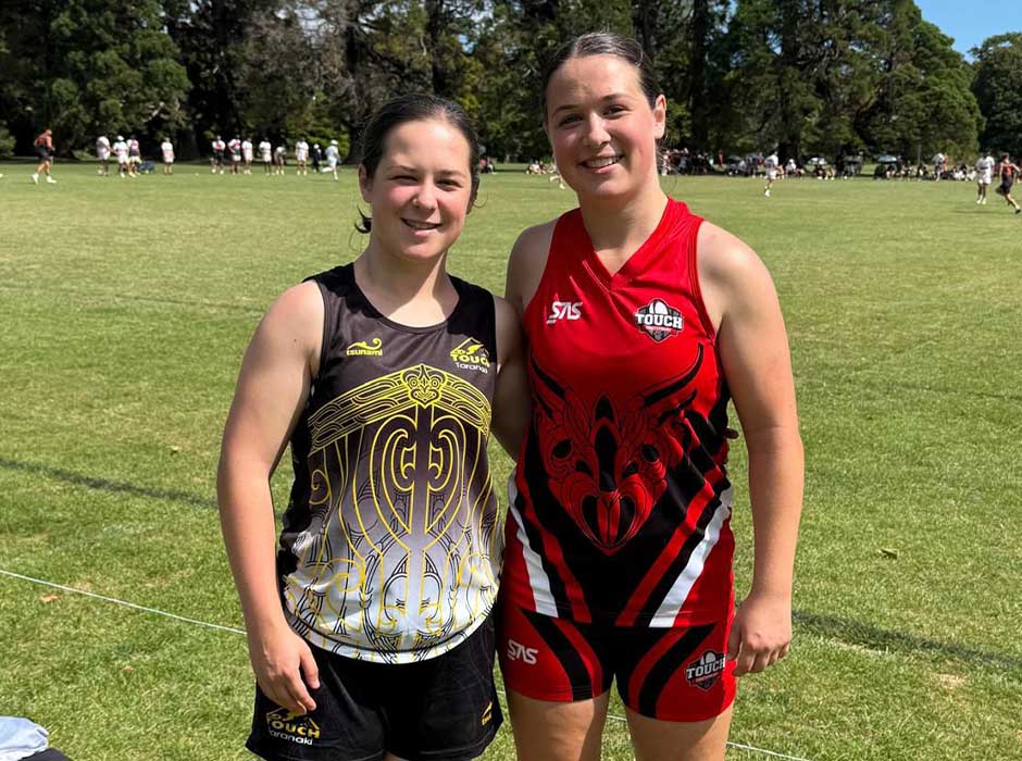 Two women standing on a sunny field wearing sports clothing 