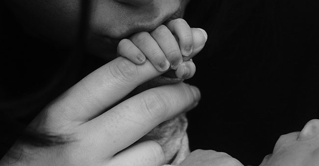 A black and white image of a baby's hand holding an adult hand 