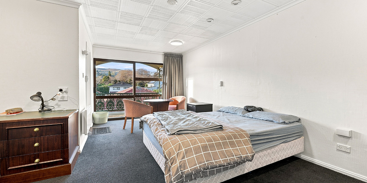 Student bedroom with double bed, sitting area and wndow view of Dunedin hills