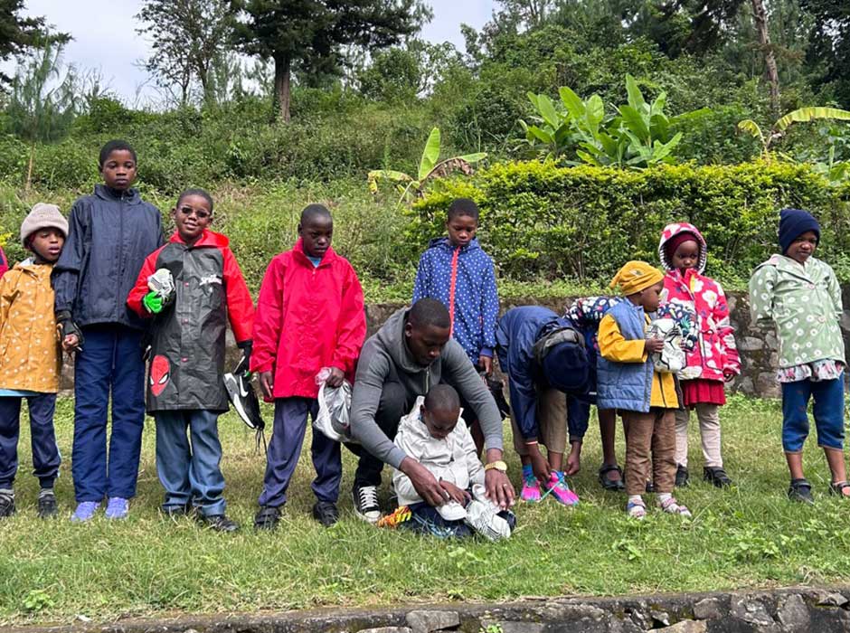 A row of children standing next to each other on grass with greenery behind them