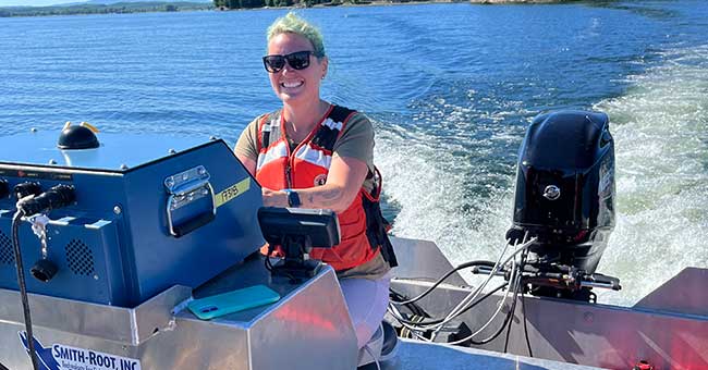 A woman steering a boat on water on a nice sunny day with land in the background