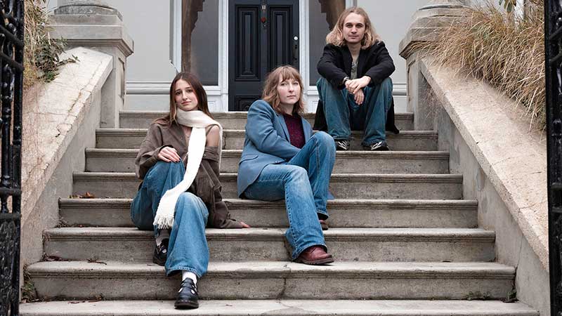 three people seated on concrete steps with a door at the top