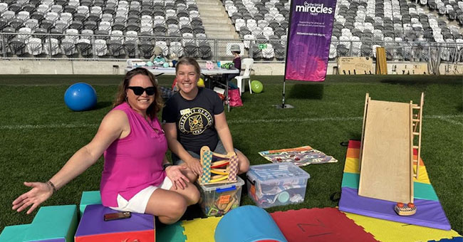Two women are pictured sitting on a blanket at a stadium.