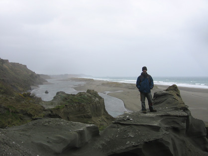 Robert Boessenecker stands on a mudstone spur by the beach. It is a gloomy overcast day