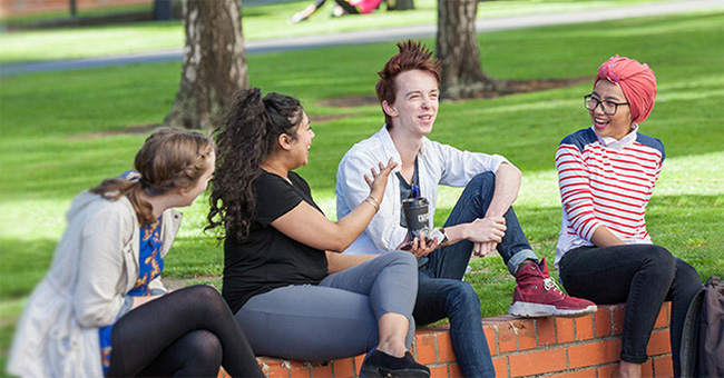 Four young people sitting on the University of Otago Union Lawn talking and laughing