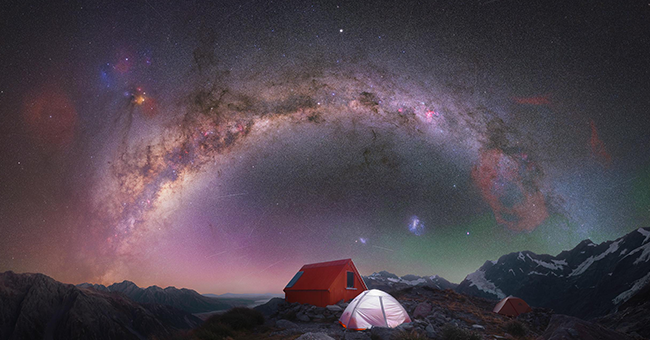 Starry sky above darkened landscape with tents