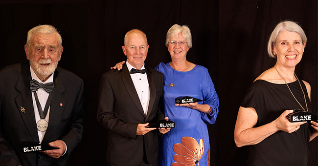 four people standing next to each other, each holding an award