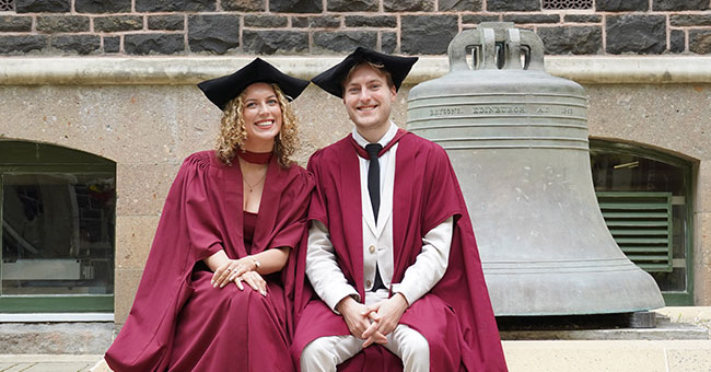 Emma-Anderson-and-Ben-Sutherland-next to bell in Uni Quad