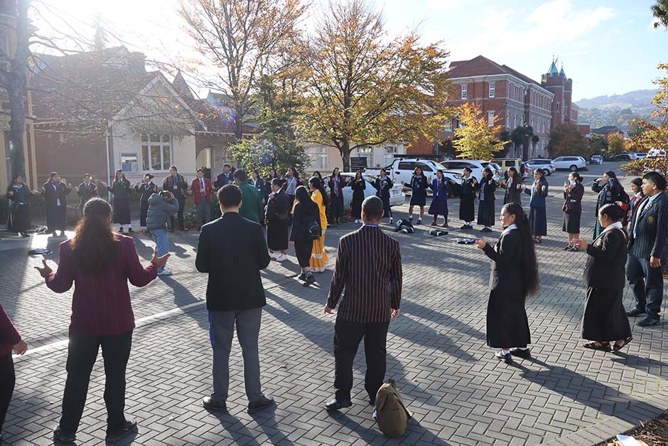 A large group of Pacific Island students in school uniforms standing in a circle outside the University of Otago's Pacific Islands Centre