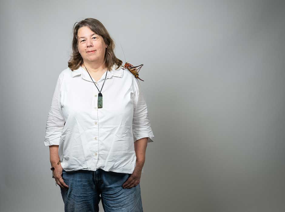 A woman wearing jeans, a white shirt and a greenstone necklace, standing in front of a blank backdrop