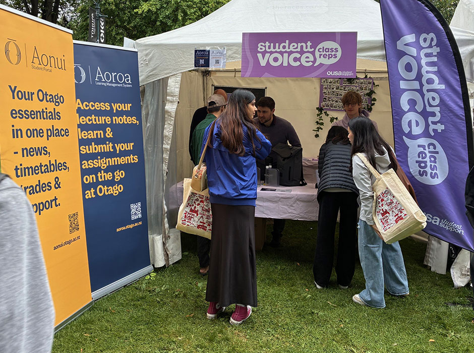 A couple of students standing in front of an information desk in a tent, at tent city, during orientation week
