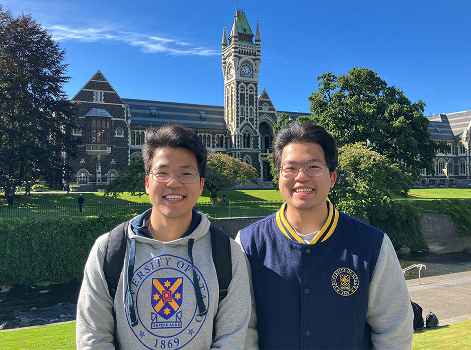 Two men standing in front of the clocktower smiling on a sunny day 