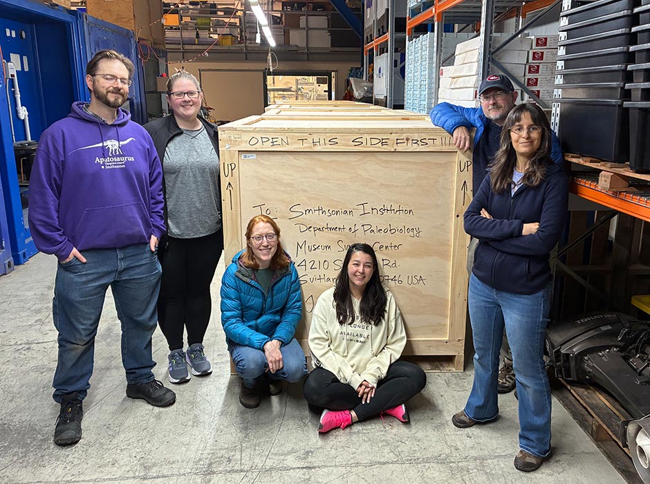 A group of people pose in front of a large wooden crate.