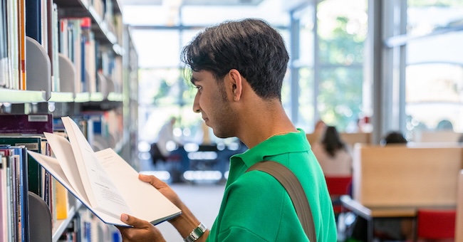 Person reading a book near library shelves