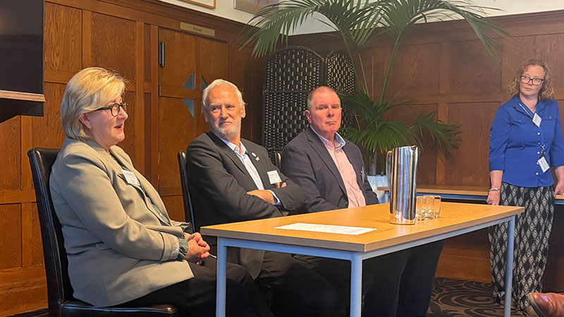A group of people - three seated at a table and one standing - at a panel discussion