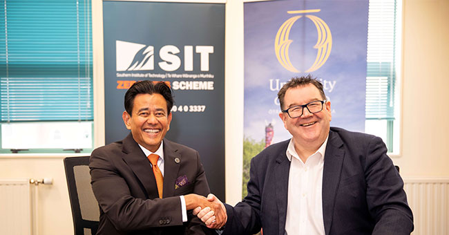 Two men seated at a table shaking hands