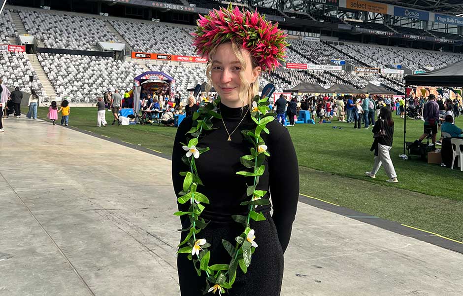 A woman standing in a stadium wearing a leafy headdress and a floral lei