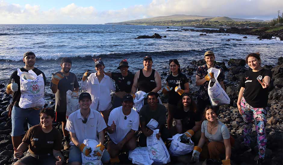 two rows of people at a beach, front row crouched down, back row standing, all smiling and holding bags that they have collected rubbish in