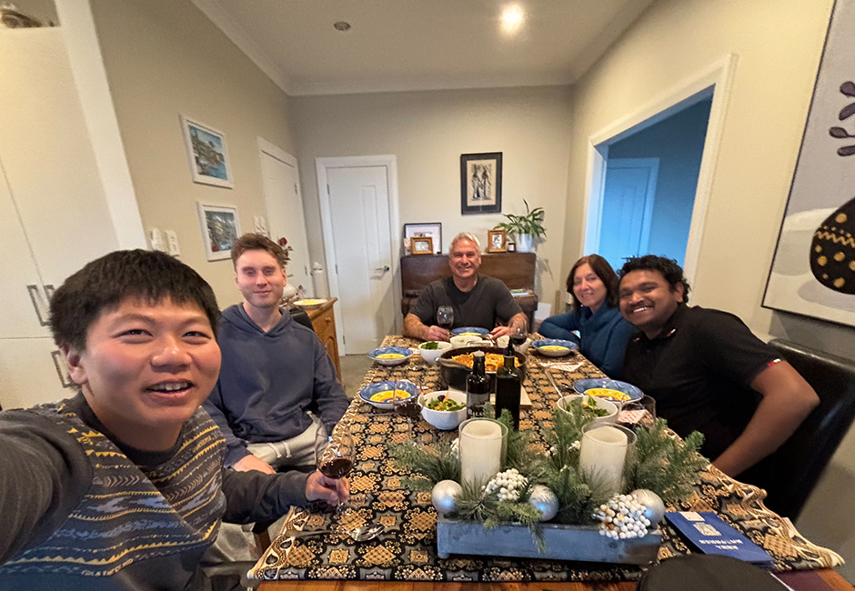Student and homestay host family sit around dining room table about to dinner.