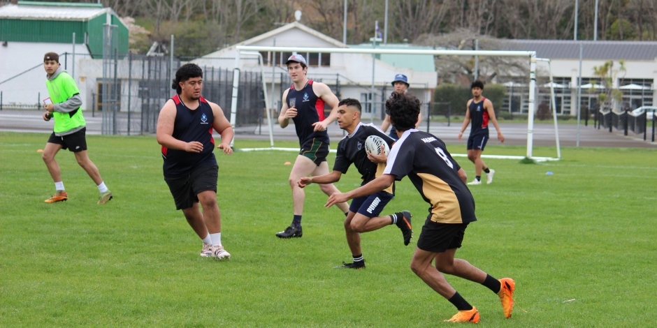 People on a field playing touch rugby. One is passing the ball just as another is reaching in to touch him.