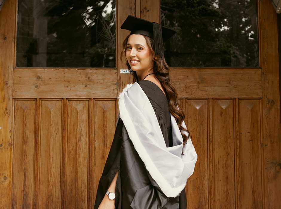 A woman standing on the clocktower steps in graduation gown