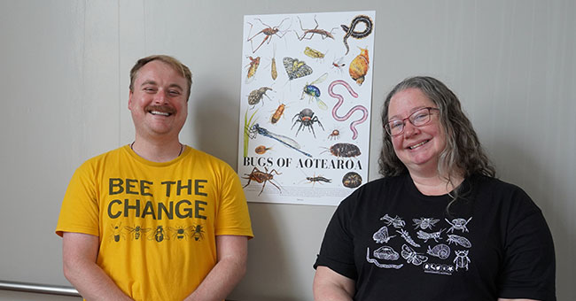 Man in yellow tee and woman in black tee standing in front of a poster of bugs