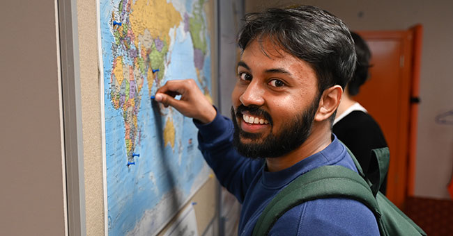 A man standing in front of a map putting a pin into it