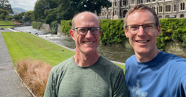 Two men standing in front of the river and clocktower